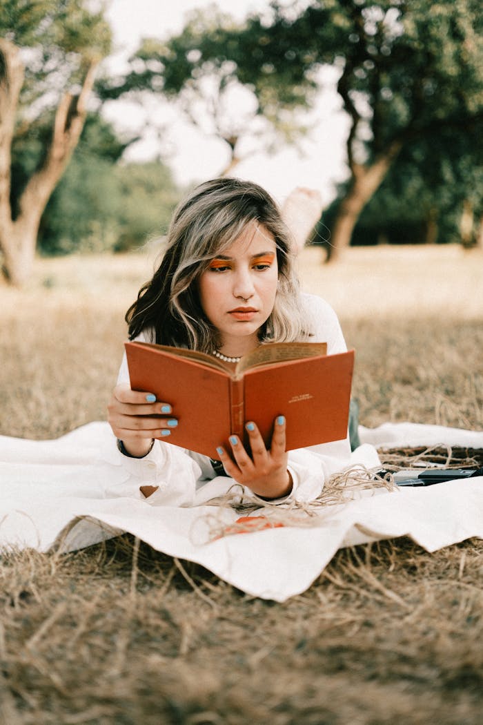 A young woman enjoys reading a book outdoors on a grassy field.